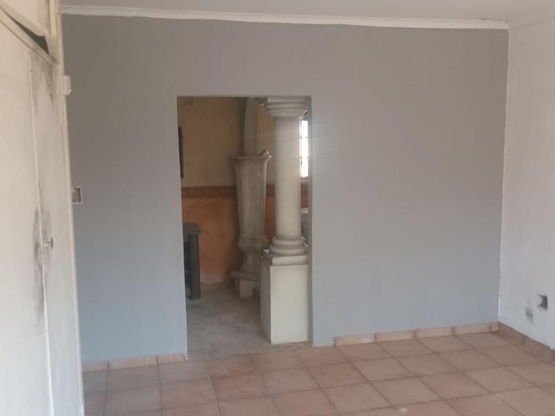 An empty living area featuring ceramic floor tiles, a decorative column, and a built-in cupboard, requiring cosmetic updates to improve its overall condition.