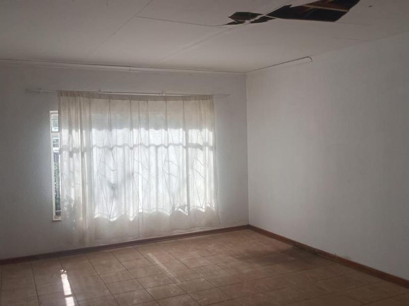 An empty living room featuring tiled flooring and a large window, currently requiring ceiling repairs.