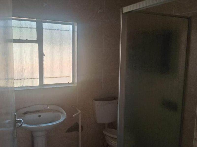 A dated bathroom featuring a pedestal basin, toilet, and shower enclosure with tiled walls, requiring renovation and cosmetic updates.