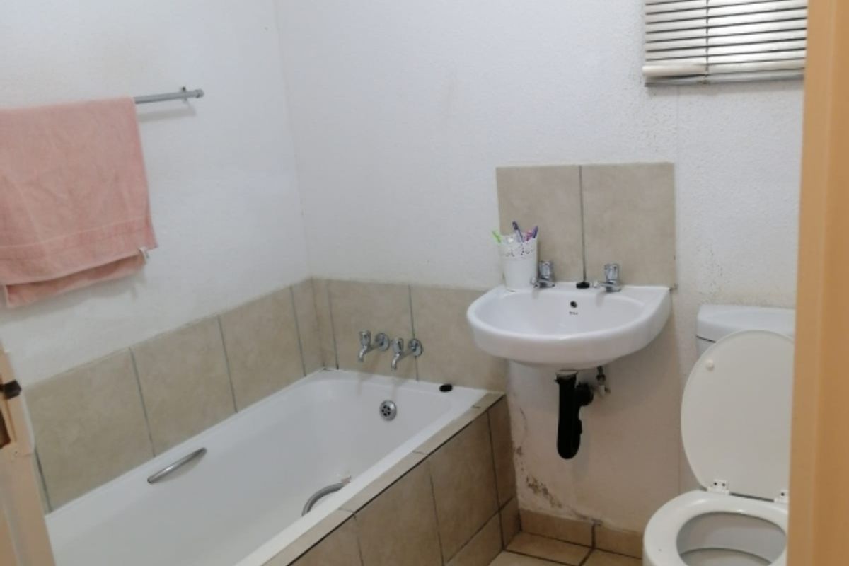 A compact bathroom featuring a bathtub, wall-mounted basin, and toilet with tiled flooring and splashbacks.