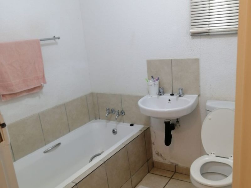 A compact bathroom featuring a bathtub, wall-mounted basin, and toilet with tiled flooring and splashbacks.