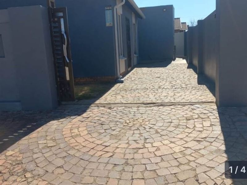A view of the front entrance featuring a patterned cobblestone driveway, secure boundary walls, and a metal gate.