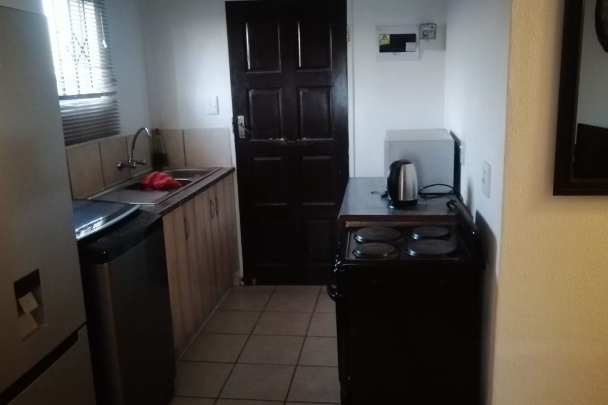 Compact kitchen featuring tiled flooring, built-in cabinetry, a stainless steel sink, and a freestanding electric stove.