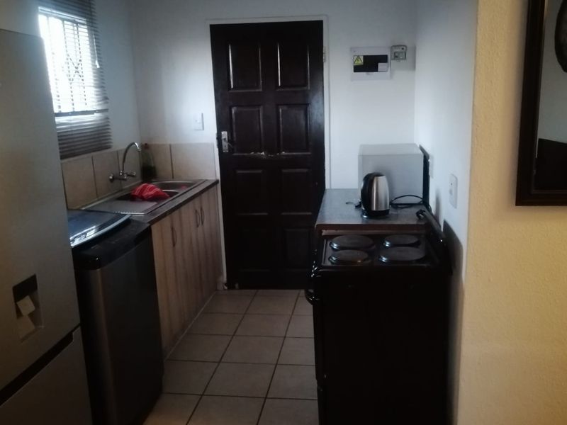 Compact kitchen featuring tiled flooring, built-in cabinetry, a stainless steel sink, and a freestanding electric stove.