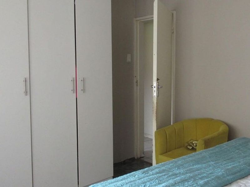 A bedroom featuring built-in cupboards and access to an adjoining room, showing signs of wear on the door and frame.