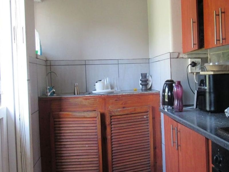 A compact scullery area featuring wooden cabinetry, tiled backsplash, and a stainless steel sink, providing functional prep and wash-up space.