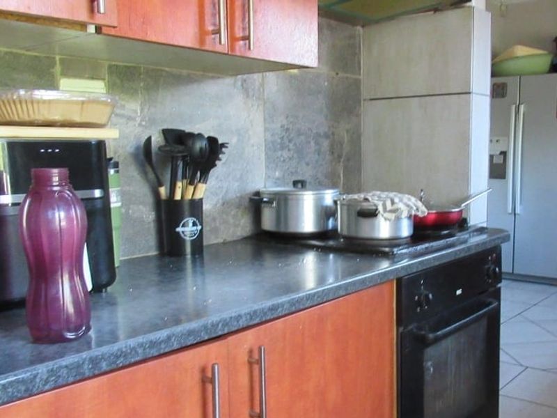 A functional kitchen featuring wood-look cabinetry, stone tile backsplash, and built-in oven with electric hob, requiring cosmetic updates to modernize the space.