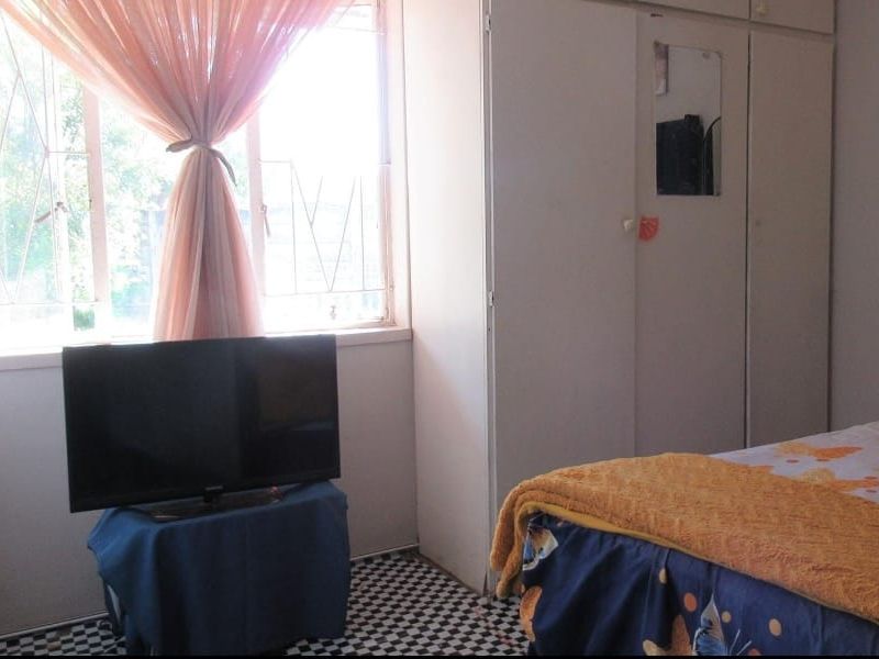 A bedroom featuring built-in cupboards and security bars on the window, providing functional storage and basic security.