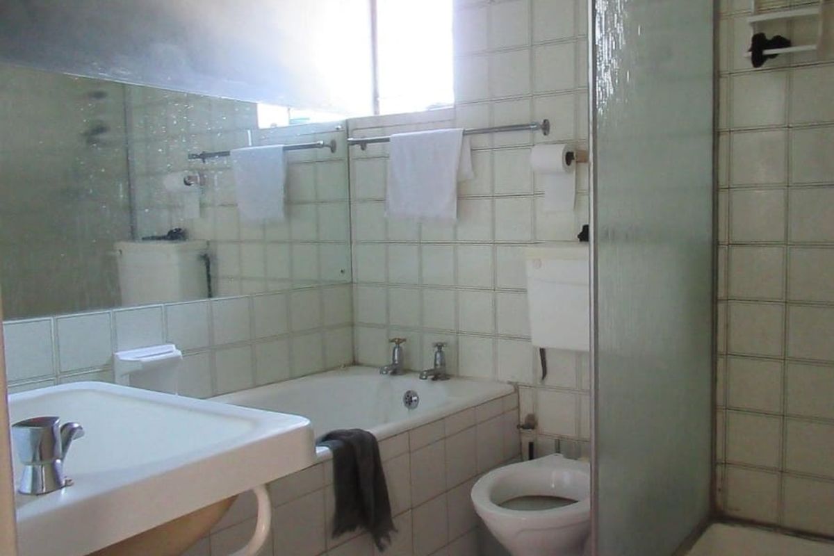 A dated bathroom featuring a bathtub, separate shower enclosure, toilet, and washbasin with wall-to-wall tiling and a large mirror.