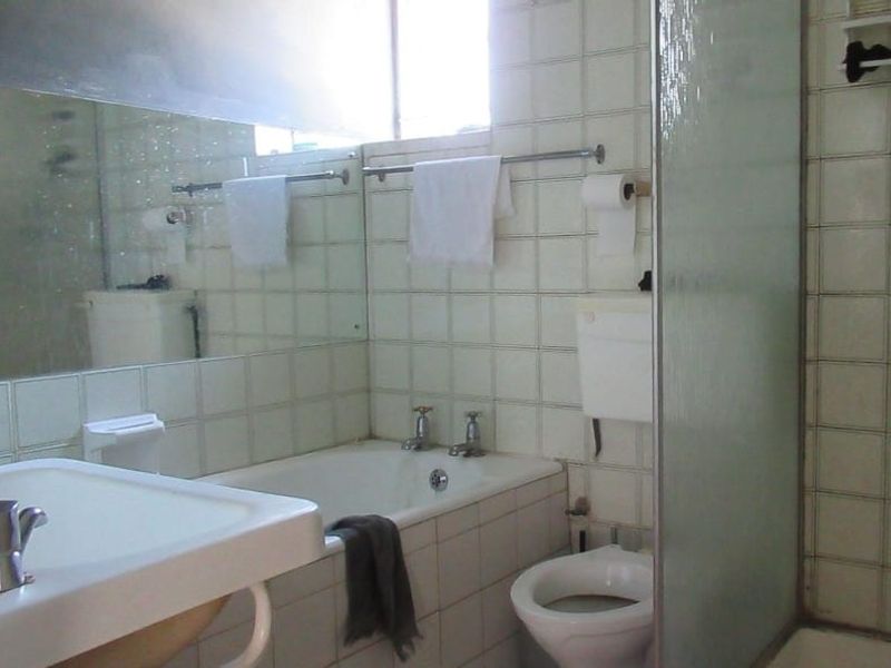 A dated bathroom featuring a bathtub, separate shower enclosure, toilet, and washbasin with wall-to-wall tiling and a large mirror.