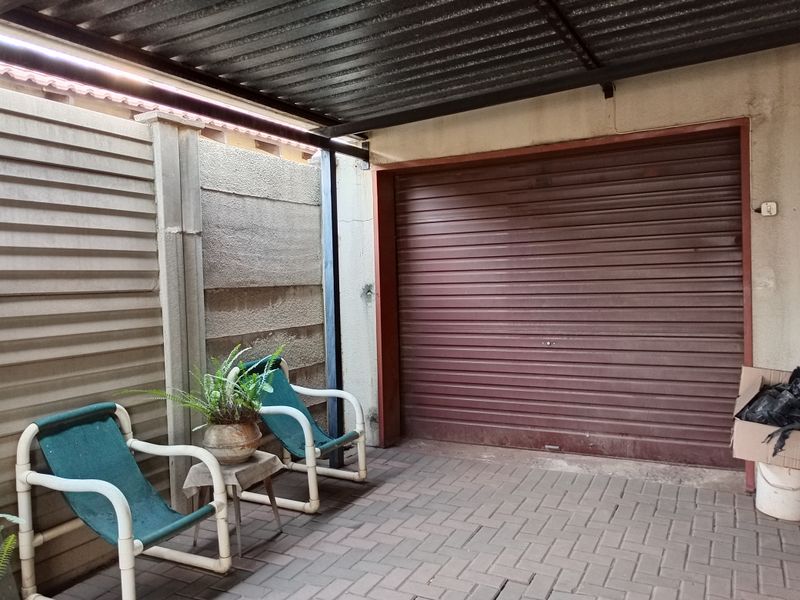 A covered garage area featuring a roller shutter door, paved flooring, and a corrugated metal roof structure.