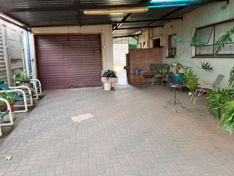 A covered outdoor garage area featuring paved flooring, a roller shutter door, and a corrugated metal roof structure.