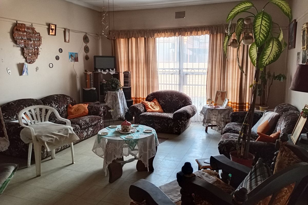 A spacious living room featuring tiled flooring, a ceiling fan, and large windows with security gates, offering a functional and comfortable living space.