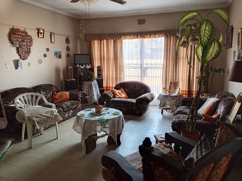 A spacious living room featuring tiled flooring, a ceiling fan, and large windows with security gates, offering a functional and comfortable living space.