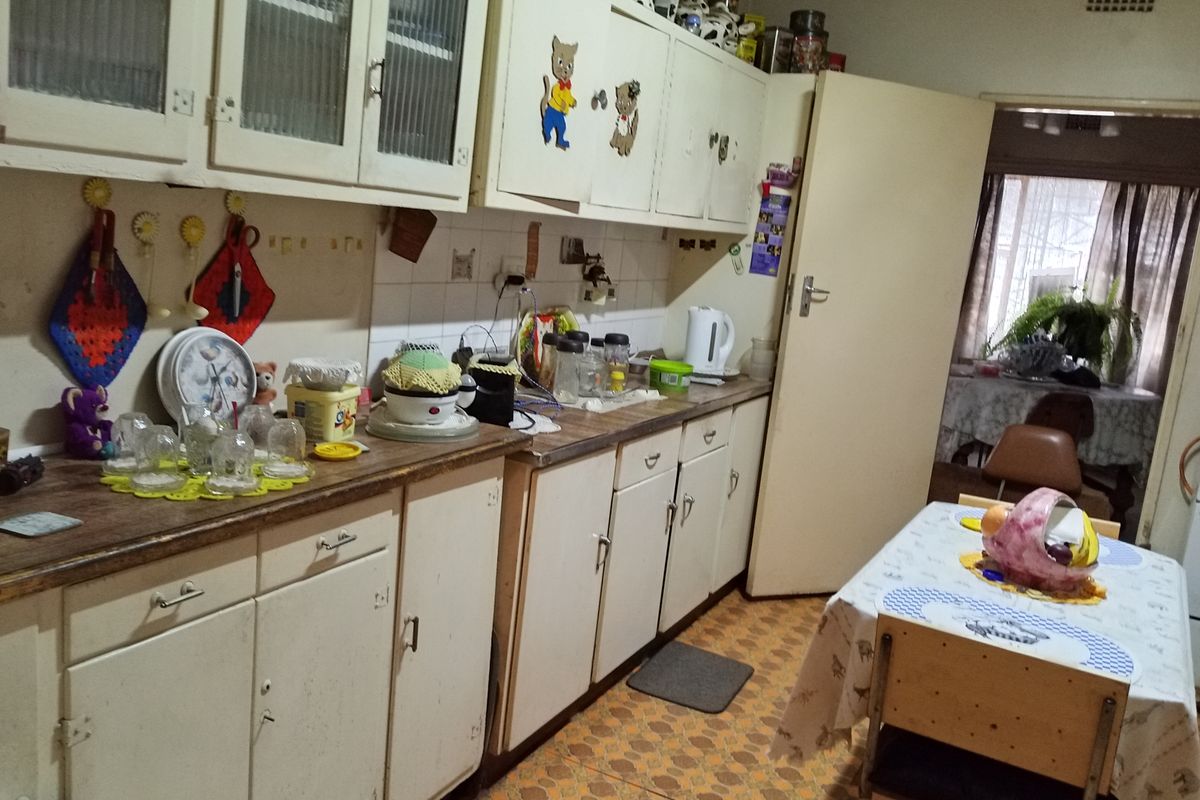 A dated kitchen featuring original built-in cabinetry, laminate countertops, and patterned vinyl flooring, offering significant potential for a modern renovation.
