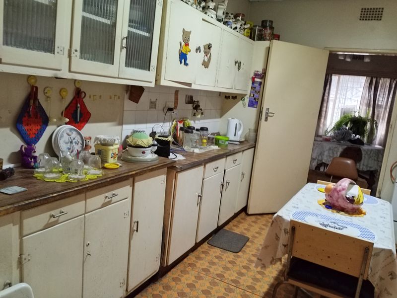 A dated kitchen featuring original built-in cabinetry, laminate countertops, and patterned vinyl flooring, offering significant potential for a modern renovation.