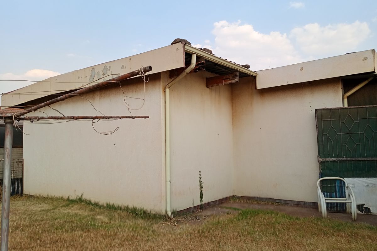 Rear exterior view of the property showing signs of significant wear, including peeling paint, stained walls, and damaged roof fascia and guttering.