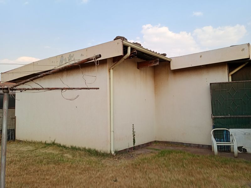 Rear exterior view of the property showing signs of significant wear, including peeling paint, stained walls, and damaged roof fascia and guttering.