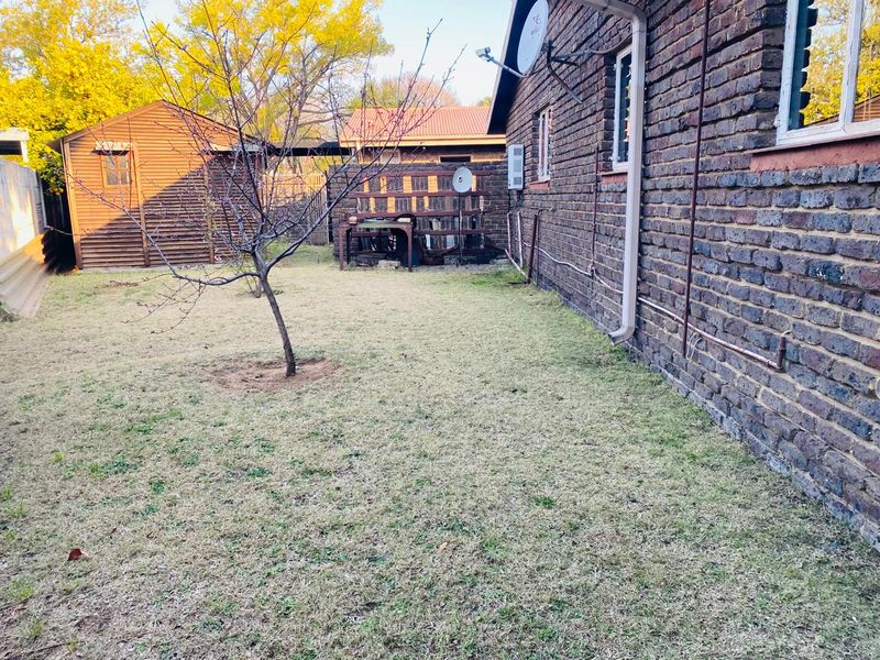 Rear garden area featuring a face brick exterior wall, satellite dish, and a detached timber storage shed.