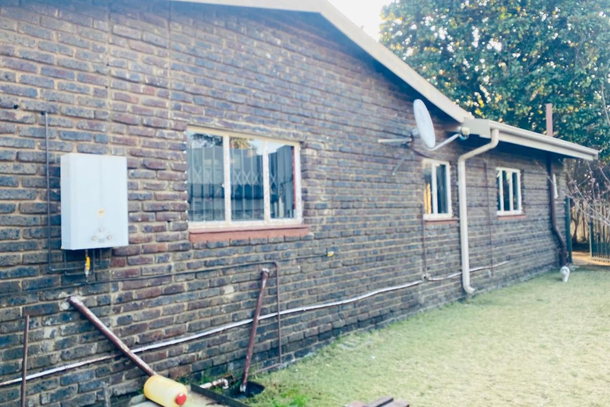 Rear exterior view of a face brick house featuring a gas geyser, security bars on windows, and an integrated guttering system.