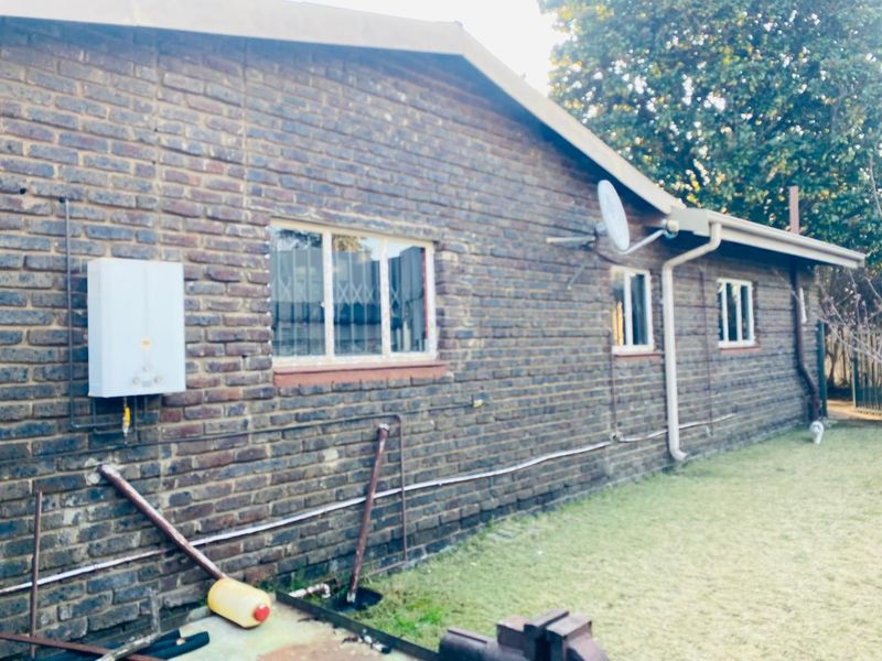 Rear exterior view of a face brick house featuring a gas geyser, security bars on windows, and an integrated guttering system.