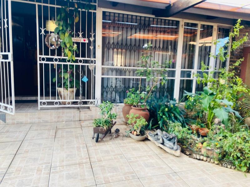 A covered patio area featuring tiled flooring, security gates, and sliding glass doors, providing a transition between the outdoor garden and the home interior.