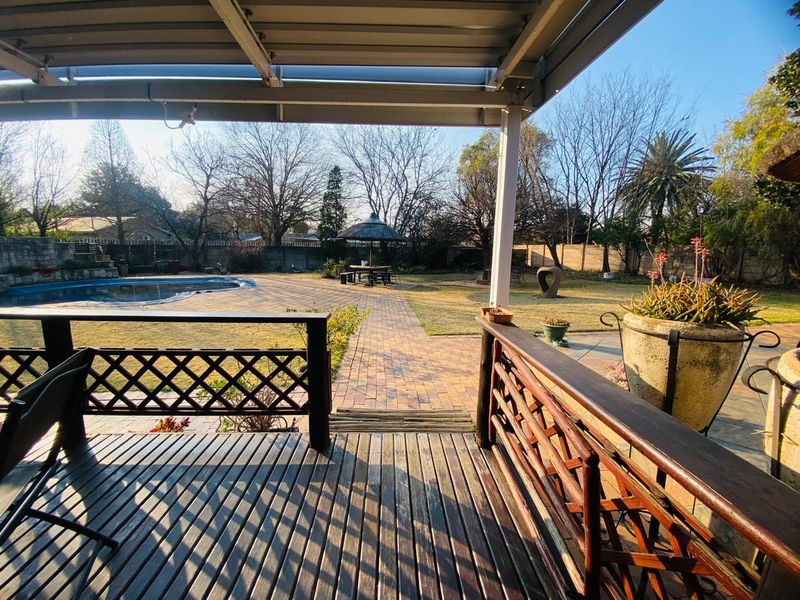 Covered timber deck patio overlooking a paved pool area and spacious garden with established trees and boundary walling.