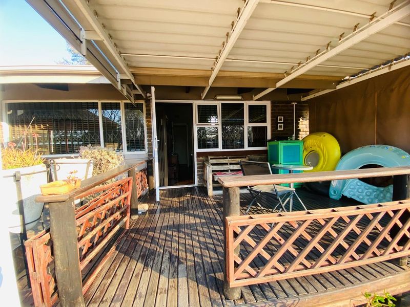 A covered outdoor timber deck patio featuring a wooden balustrade and direct access to the main house through a glass door.