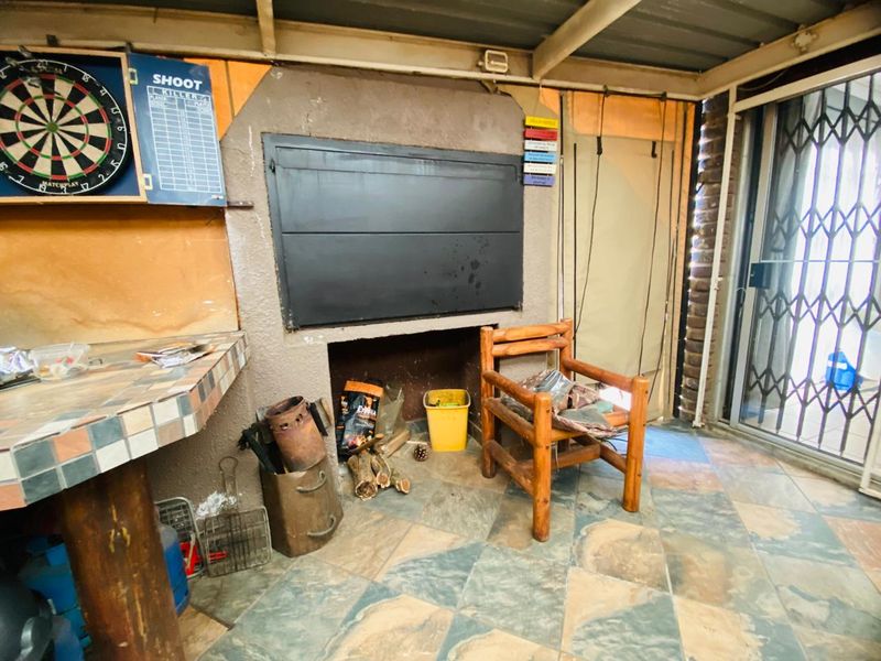 Covered outdoor patio area featuring a built-in braai, tiled flooring, and direct access to the home via a security gate.