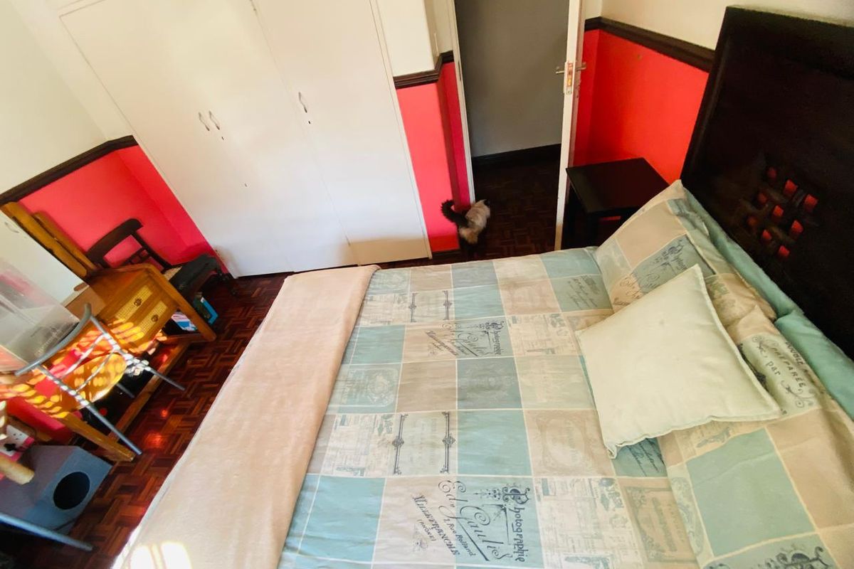 A bedroom featuring parquet flooring, built-in cupboards, and a dado rail, offering a functional space with potential for cosmetic updates.