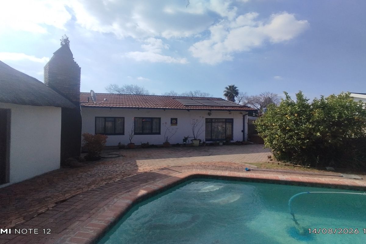 Rear exterior view of the property featuring a swimming pool, brick paved patio area, and a combination of tiled and thatched roofing.