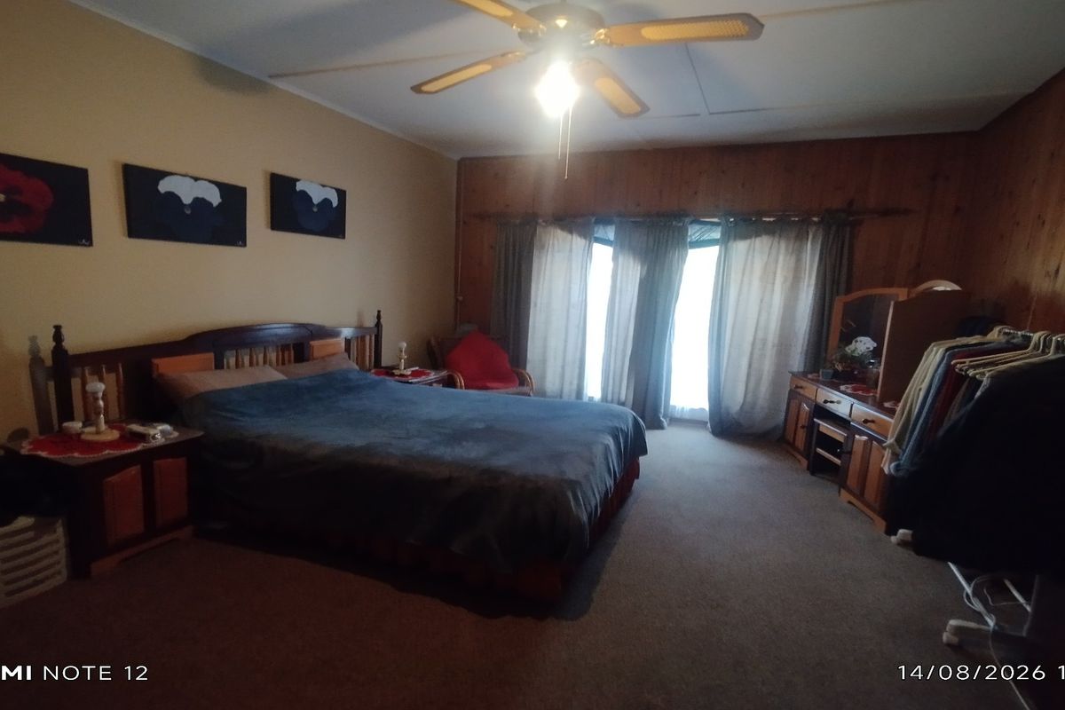 A spacious bedroom featuring wood paneling, a ceiling fan, and a built-in vanity area with natural light from the window.