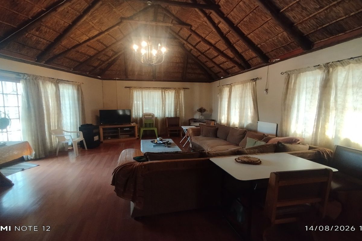 Spacious living area featuring a high vaulted thatched ceiling with exposed timber rafters and laminate flooring, offering a rustic and open atmosphere.