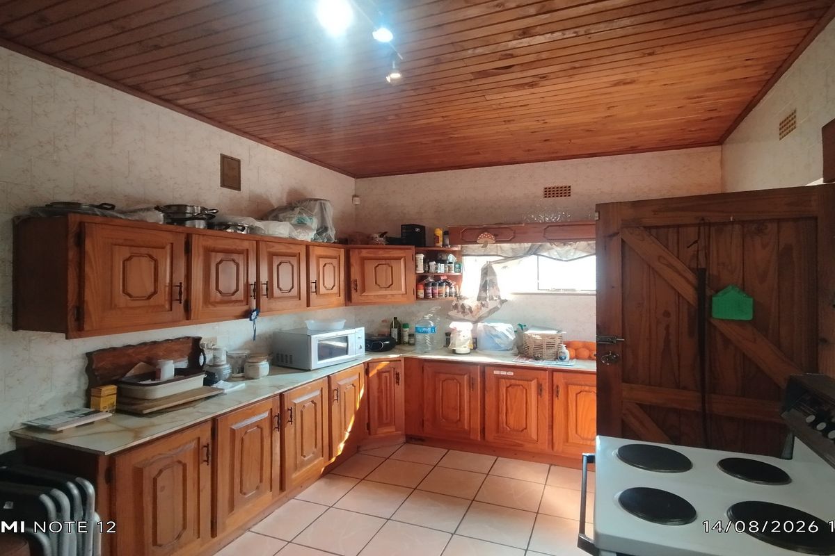 A functional kitchen featuring traditional wooden cabinetry, tiled flooring, and a warm timber-paneled ceiling, offering a classic, dated aesthetic ready for modernization.