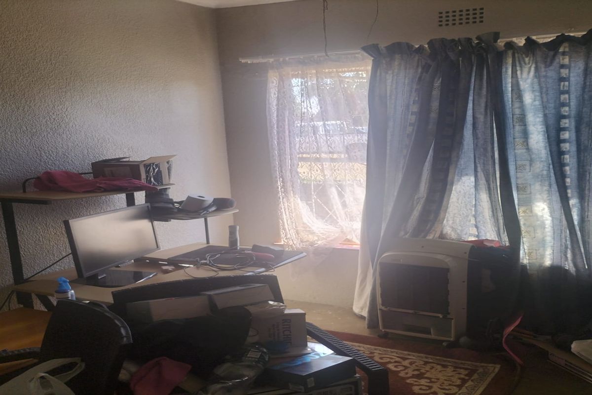 A bedroom featuring textured walls and a window with curtain rails, currently showing signs of wear and exposed electrical wiring.