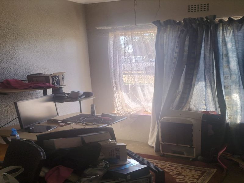 A bedroom featuring textured walls and a window with curtain rails, currently showing signs of wear and exposed electrical wiring.