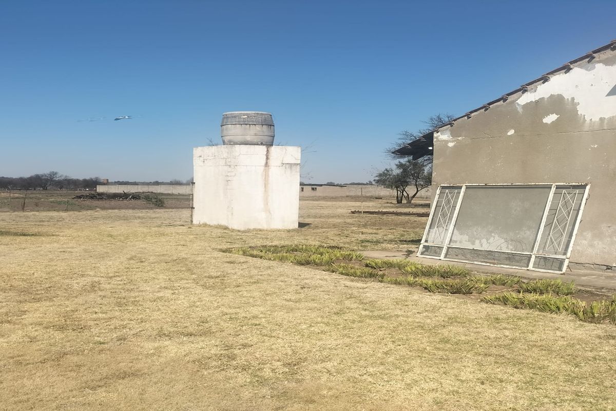 Rear exterior view of the small holding featuring a water storage tank on a concrete plinth and a building with visible exterior wall damage.