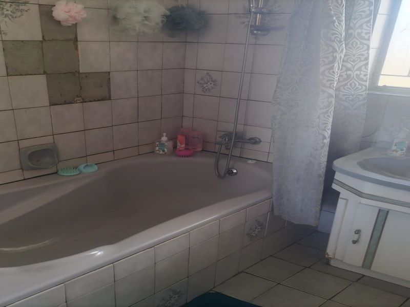 A dated bathroom featuring a built-in bathtub with shower mixer, vanity cabinet, and tiled finishes, currently requiring maintenance and cosmetic updates.