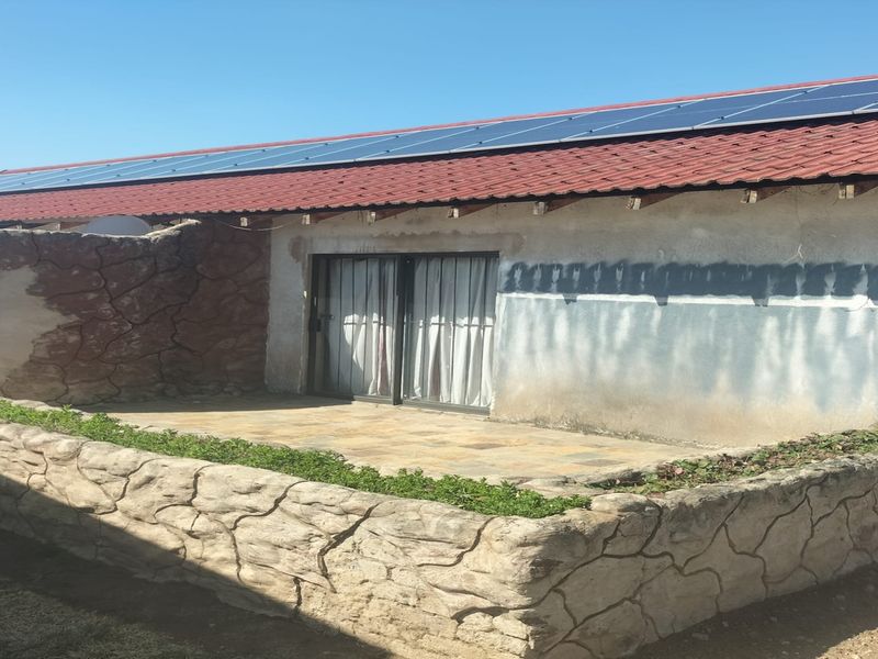 Outdoor patio area featuring stone cladding retaining walls, sliding door access, and roof-mounted solar panels on a tiled roof structure.