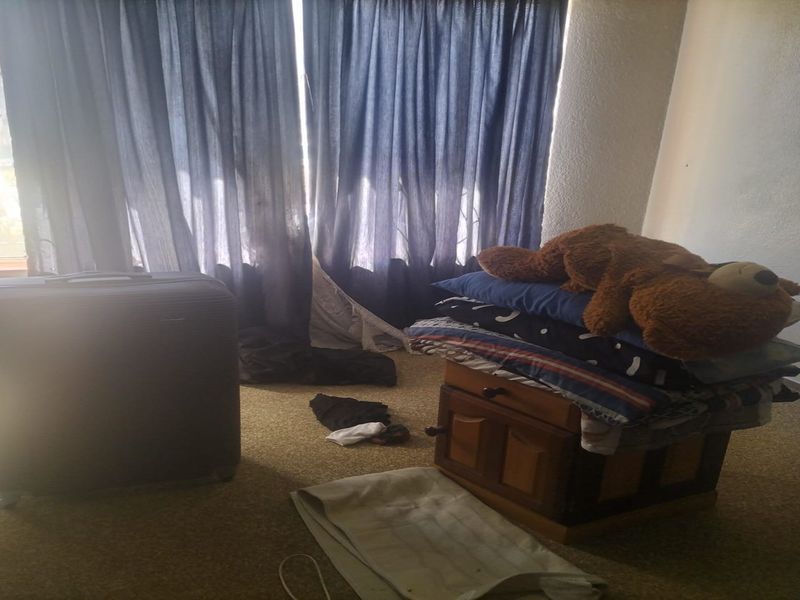 A bedroom space featuring carpeted flooring and window curtain rails, currently used for storage.