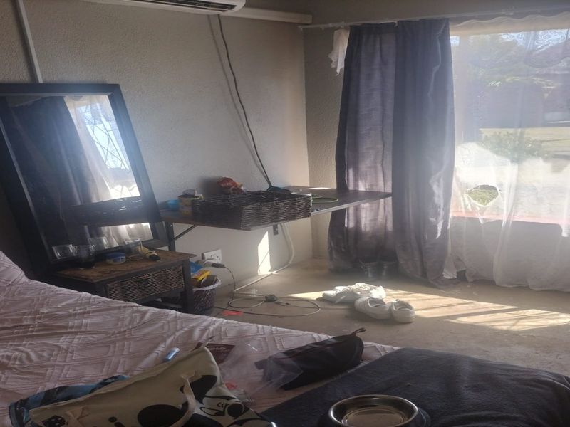 A bedroom featuring an air conditioning unit and large window with natural light, currently requiring maintenance to finishes and fixtures.