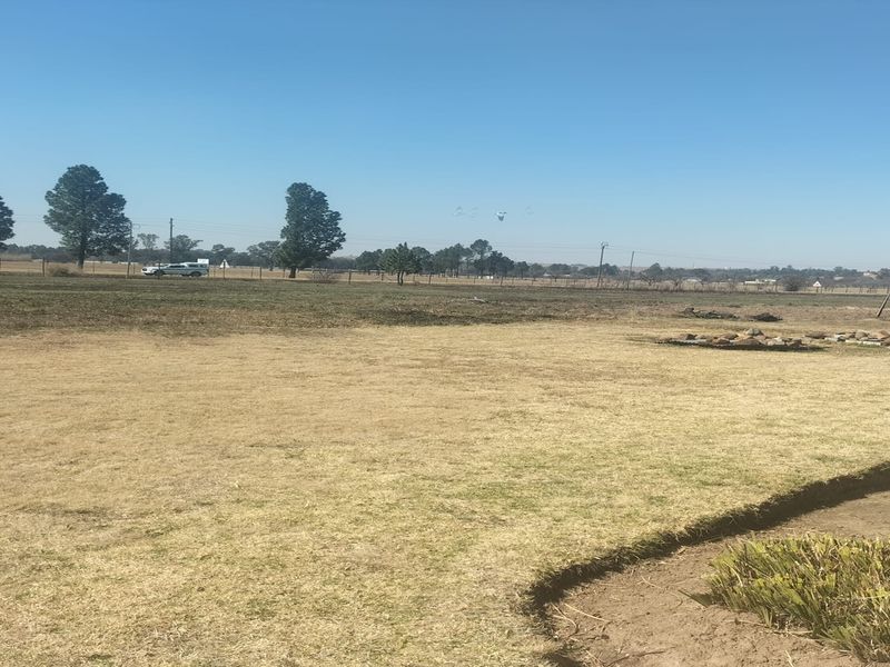 A wide-angle view of a large, dry garden area on a small holding, featuring open lawn space and perimeter fencing.