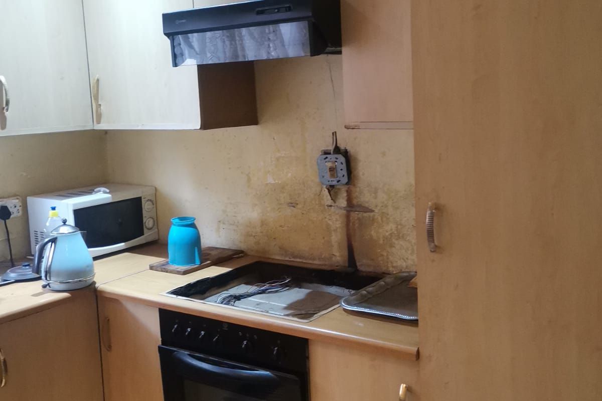 A dated kitchen featuring built-in cabinetry, an electric oven, and hob, requiring cosmetic updates and repairs to the wall and electrical fixtures.