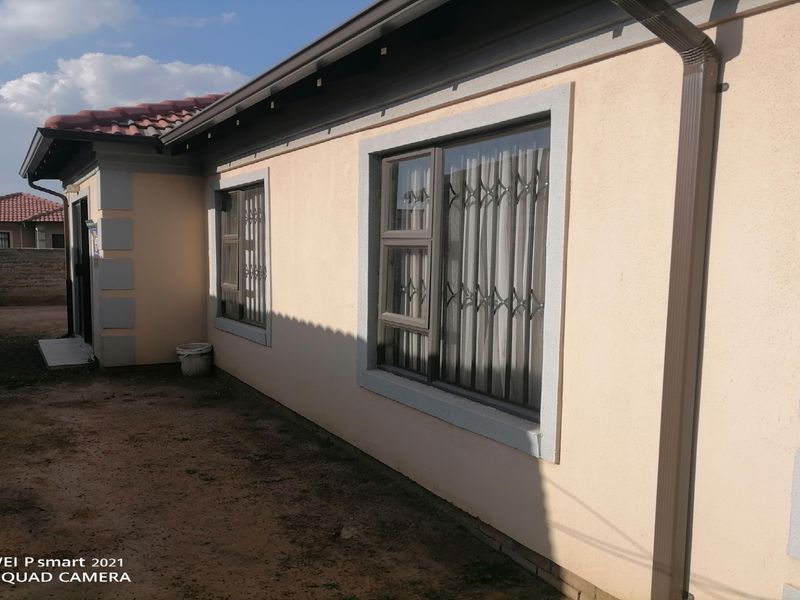 A view of the rear exterior of the house featuring plastered walls, aluminium window frames with security bars, and a tiled roof.