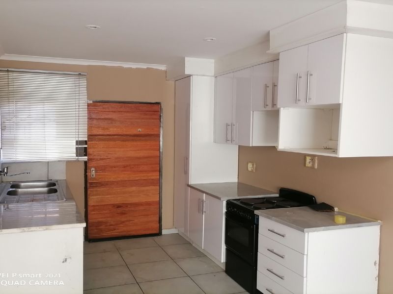 A functional kitchen featuring white cabinetry, a double sink, and an electric stove, with tiled flooring and neutral wall tones.