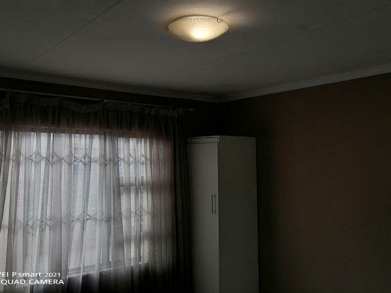 A bedroom featuring a built-in wardrobe, window with security gate, and ceiling light fixture. The room has dark wall finishes.