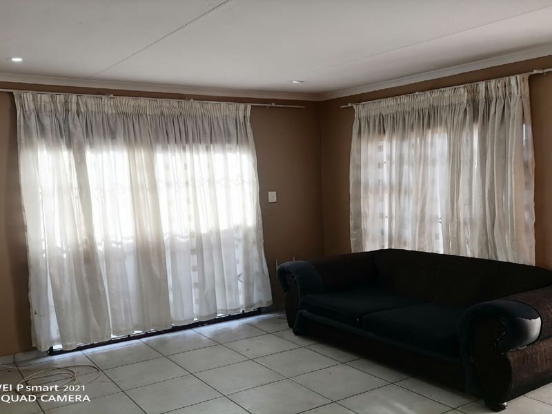 A living room featuring tiled flooring, recessed downlights, and large windows with security gates and curtain rails.