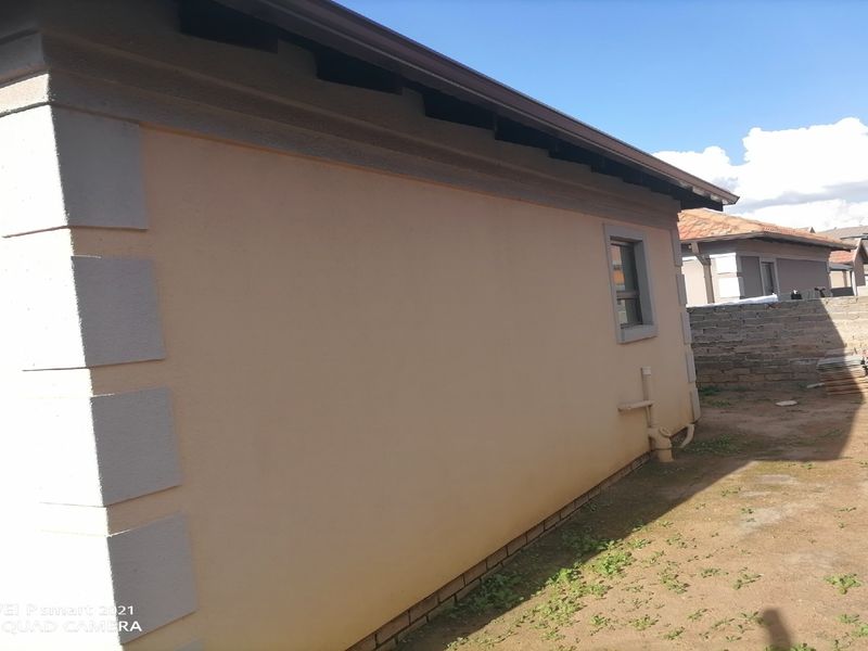 A view of the rear exterior wall of the house, featuring painted plaster finish, guttering, and a surrounding brick boundary wall.