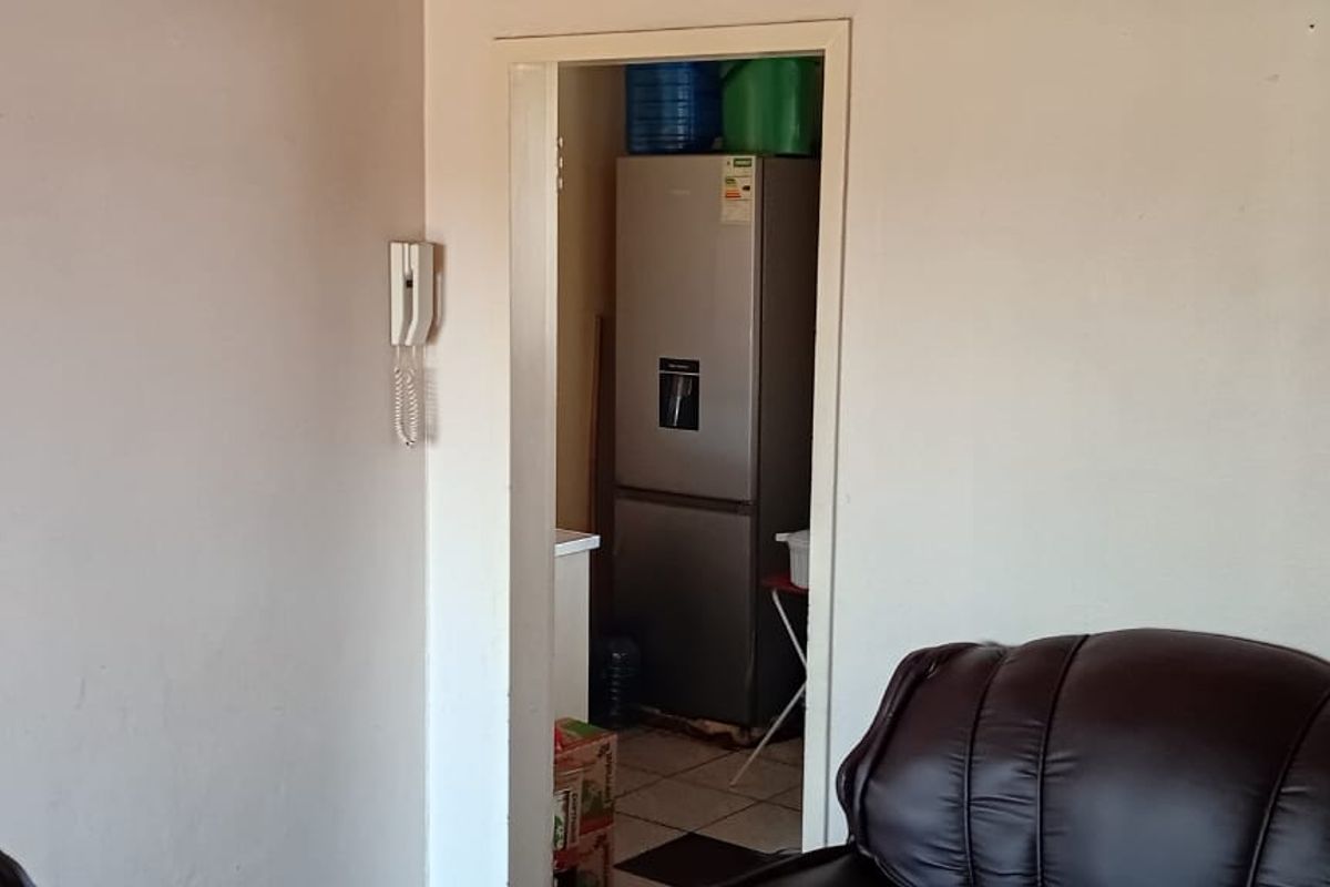 A view through a doorway into a utility or scullery area, featuring tiled flooring and an intercom system mounted on the adjacent wall.