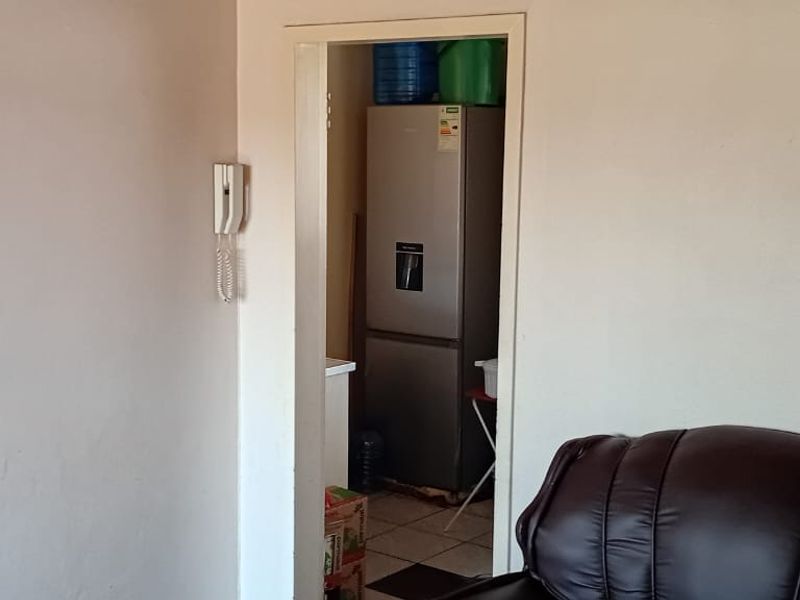 A view through a doorway into a utility or scullery area, featuring tiled flooring and an intercom system mounted on the adjacent wall.